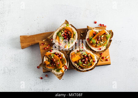 Snack vari tipi di pane con hummus e zucca cotta su una scheda che serve con pesto di rucola. i semi di melograno e pinoli. cibo sano Foto Stock