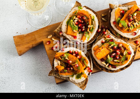 Snack vari tipi di pane con hummus e zucca cotta su una scheda che serve con pesto di rucola. i semi di melograno e pinoli. cibo sano e vino bianco Foto Stock