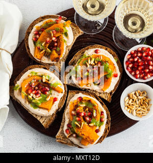 Snack vari tipi di pane con hummus e zucca cotta su una scheda che serve con pesto di rucola. i semi di melograno e pinoli. cibo sano e vino bianco Foto Stock