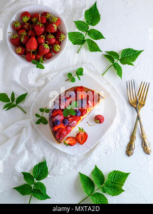 La metà di un grafico a torta di ricotta e fragole fresche, vicino a due forcelle di ferro, sfondo bianco, vista dall'alto Foto Stock