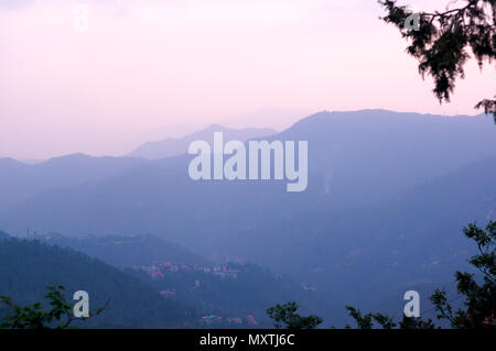 Blue Hills con alberi su di essi dissolvenza in entrata la distanza e la rosa cielo incandescente di crepuscolo shot in Shimla. Vetrine la tranquillità e la bellezza del luogo Foto Stock