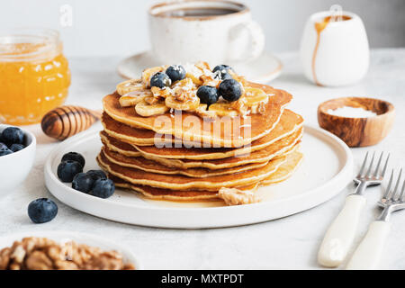 Frittelle con noci, miele e frutti per la prima colazione. Pila di frittelle americane. Gustose frittelle sulla piastra bianca, vista ingrandita, il fuoco selettivo Foto Stock