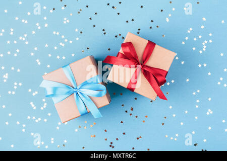 Due confezioni regalo avvolti in carta kraft e legate con nastro su sfondo blu decorato con coriandoli. Vista superiore, idea regalo per Lui e per lei. Foto Stock