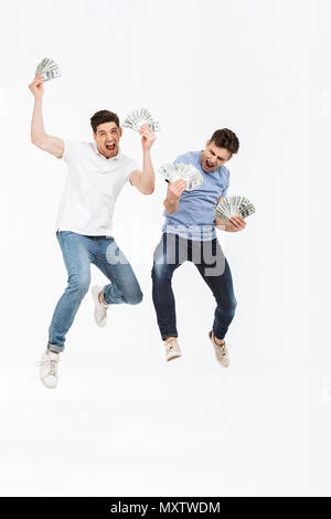 A piena lunghezza ritratto di due giovani felici uomini che mostra le banconote denaro e celebrare il successo durante il salto isolate su sfondo bianco Foto Stock