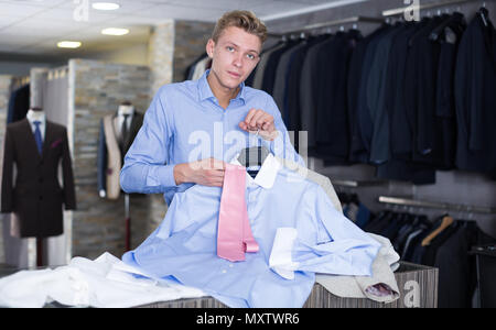 Acquirente maschio in camicia scegliendo cravatta e camicia nel negozio di abbigliamento Foto Stock