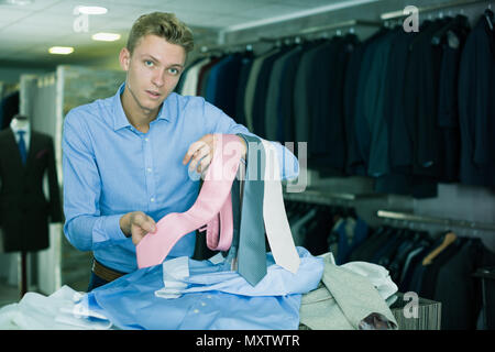 Maschio adulto acquirente in camicia scegliendo il tirante in negozio di abbigliamento Foto Stock