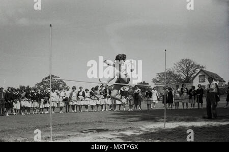 1960, foto storiche di secondaria schoogirl prendendo parte ad un inter-scuola county giornata di sport, Dorset, Inghilterra, Regno Unito. Qui possiamo vedere la sua fare il salto in alto con un piuttosto uno stile individuale e sorvegliato da una linea di spectatotrs. Foto Stock