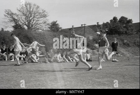 1960, foto storiche, secondario di scolari di prendere parte ad un inter-scuola county giornata di sport, Dorset, Inghilterra, Regno Unito. Qui li vediamo in competizione in un relè del team in gara su una pista in erba, come le guide passare il testimone al loro compagno di squadra per la prossima tappa della gara. Foto Stock