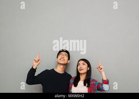 Immagine di entusiasti giovani asiatici amare giovane standing isolate su muro grigio Sfondo cercando riposo rivolto verso l. Foto Stock