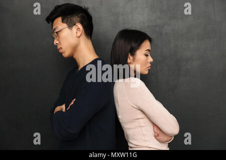 Vista laterale di offeso asian giovane in piedi indietro per ogni altro con bracci incrociati su sfondo nero Foto Stock