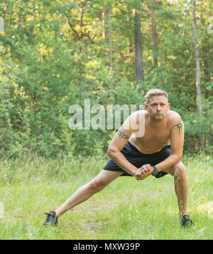 Barechested metà adulto 40s uomo caucasico facendo si allunga la gamba prima di esercizio Foto Stock