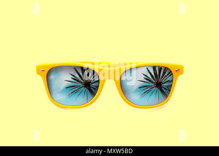 Estate Concetto di immagine: giallo occhiali da sole con Palm tree riflessioni isolato in colore pastello giallo dello sfondo. Immagine minimalista pronto per l'estate, sun protec Foto Stock