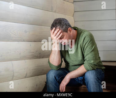 Triste Caucasian uomo di mezza età seduta sulle scale all'interno della casa Foto Stock