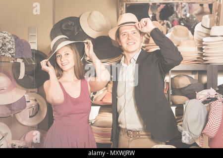 Felice inglese giovane moglie e marito scegliendo dress cappelli in negozio Foto Stock