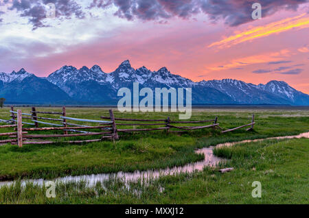 Tramonto a Teton Range - una molla vista al tramonto del Teton Range, con rampa arrugginito recinzioni e avvolgimento del flusso di drenaggio di un vecchio ranch in fila Mormone nella parte anteriore. Foto Stock