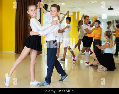 I bambini di studiare nuove danze di coppia con il giovane allenatore femmina nella classe di danza Foto Stock