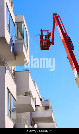 Uomo facciata di pulizia di un moderno stile minimalista appartamento edificio su un braccio telescopico elevatore utilizzando la pressione di lavaggio a getto con cielo blu sullo sfondo Foto Stock
