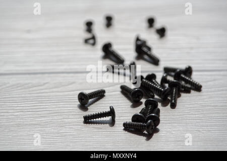 Piccole viti nere sono sparse su sfondo di legno Foto Stock