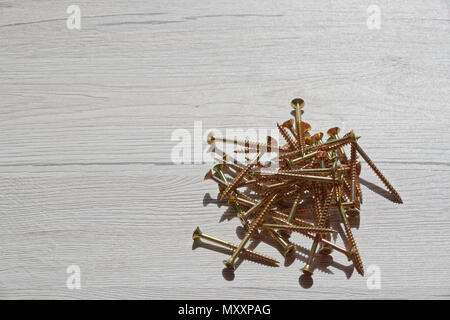 Pila di giallo lucido viti sul grigio Sfondo di legno Foto Stock