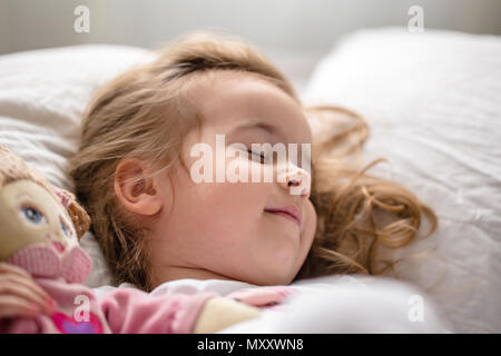 Una bambina si addormenta nel letto con Soffice bambola, letto bianco Foto Stock