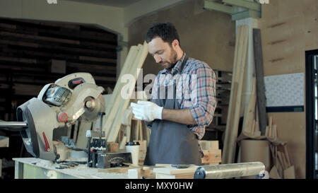 Carpenter in piedi vicino a sega elettrica nel suo laboratorio e di bere il caffè. Foto Stock