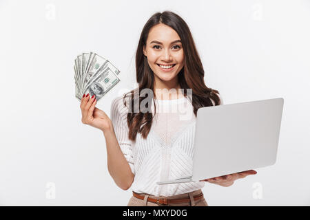 Ritratto di un sorridente asian imprenditrice che mostra le banconote denaro tenendo premuto il computer portatile isolato su sfondo bianco Foto Stock