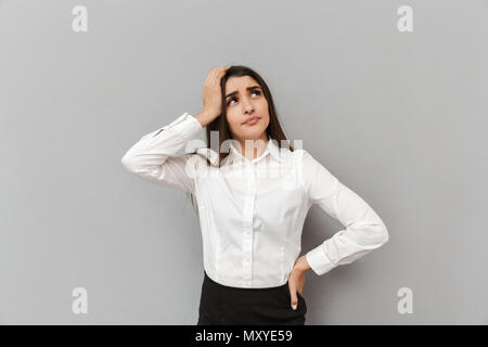 Ritratto di giovane premuroso office donna con la cova guardare in maglia bianca guardando verso l'alto e toccando la sua testa isolate su uno sfondo grigio Foto Stock