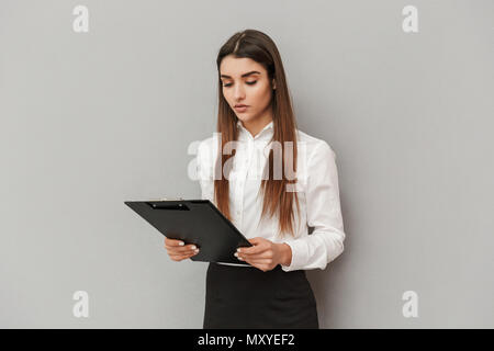 Foto di grave donna in camicia bianca e gonna nera tenendo appunti con i documenti di office isolate su uno sfondo grigio Foto Stock