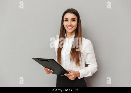 Foto di donna sorridente in una camicia bianca e gonna nera tenendo appunti con i documenti di office isolate su uno sfondo grigio Foto Stock
