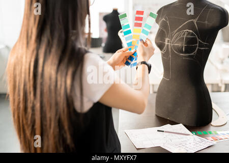 Vista posteriore ritratto di focalizzata donna asiatica che lavorano in fashion design la scelta di una tavolozza dei colori dei campioni di trattenimento permanente al tavolo mediante cucitura in dummy e moderno. Foto Stock