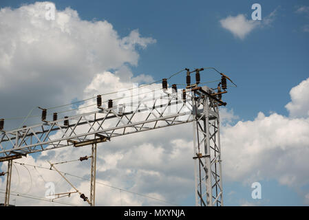 Stazione ferroviaria o linea di alimentazione supporto. Alimentazione ferroviario con le linee elettriche in alta tensione su pali metallici contro il cielo blu. Foto Stock