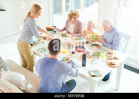 Ritratto di felice due famiglia di generazione di gustare la cena insieme seduti a tavola festiva con deliziosi piatti durante la celebrazione di vacanza in sunli Foto Stock