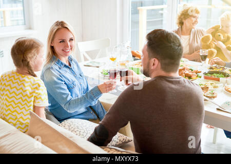 Ritratto di felice donna bionda tintinnanti bicchieri di vino con mio marito durante la cena di famiglia in presenza di luce solare Foto Stock