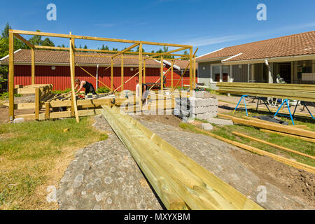 Falegnami per lavorare in esterno a erigere un grande patio con pergola e round firepit Foto Stock