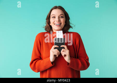 Ritratto di un entusiasta giovane donna vestita di maglione holding passaporto con i biglietti di volo isolate su sfondo blu Foto Stock