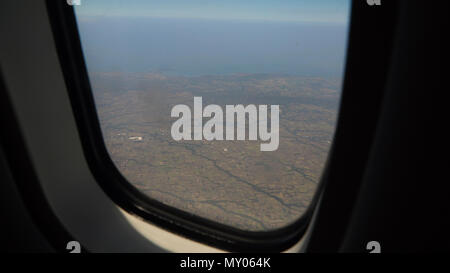 Vista attraverso un aereo finestra sull'isola tropicale, oceano e Cielo e nubi. Vista aerea del mare, le nuvole e il cielo come visto attraverso la finestra di un aeromobile. Concetto di viaggio. Foto Stock