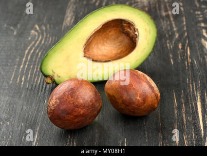 Due semi di avocado con metà su sfondo di legno Foto Stock