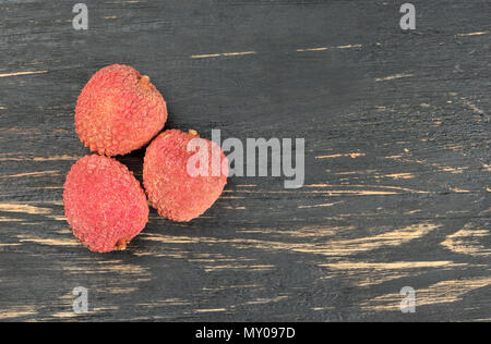 Tre lychee cinese frutto su un vuoto sullo sfondo di legno, vista dall'alto Foto Stock