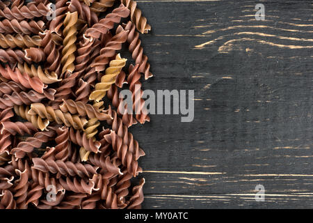 Sparse scuro fusilli di pasta su un vuoto sullo sfondo di legno Foto Stock