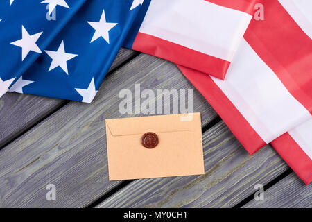 Bandiera americana e la busta di artigianato. Bandiera degli Stati Uniti e in stile vintage busta con sigillo di cera rossa timbro su tavole di legno, vista dall'alto. Foto Stock