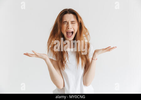 Foto di Angry donna in t-shirt urlando con gli occhi chiusi su sfondo grigio Foto Stock