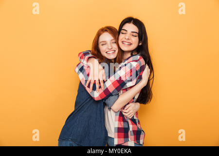 Ritratto di due lieti di giovani ragazze adolescenti abbracciando isolate su sfondo giallo Foto Stock