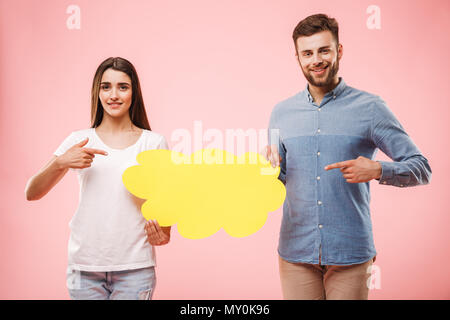 Ritratto di un sorridente coppia giovane puntare il dito a vuoto discorso bolla isolate su sfondo rosa Foto Stock
