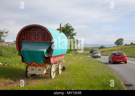 Carovane zingare rom, vagoni vanner, vardo, carovane a prua, carro tradizionale trainato da cavalli, carretti decorati con decorazioni e alloggi a Kirkby Stephen, Cumbria. I membri della comunità itinerante si dirigono alla Appleby Horse Fair mentre le strade in Cumbria e nelle Yorkshire Dales preparano il pascolo per i loro cavalli di cocco durante il loro raduno annuale. La fiera dei cavalli si tiene ogni anno all'inizio di giugno. Attrae circa 10.000 zingari e viaggiatori e circa 30.000 altre persone. Piuttosto che un evento organizzato con un programma fisso, viene pubblicizzato come la più grande fiera zingara tradizionale Foto Stock