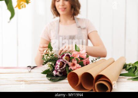 Foto sfocate della giovane donna di fiorista raccolta di bouquet di fiori diversi sulla tavola in officina Foto Stock
