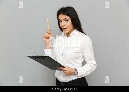 Ritratto di donna di successo con lunghi capelli scuri che indossa pragmatico outfit holding appunti con documenti ed esaminando i documenti isolate su grigio Foto Stock