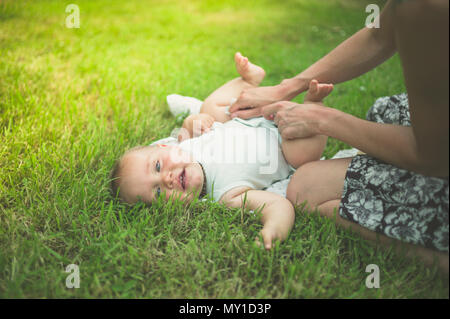 Una giovane madre sta cambiando il suo bimbo di pannolino sul prato di natura Foto Stock