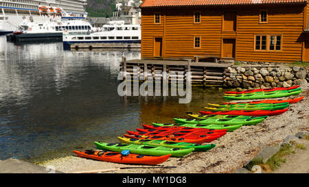 Canoe colorate lungo la spiaggia di fronte a una casa marrone. I traghetti e la nave di crociera in background. Ubicazione Eidfjord in Hordaland, Norvegia. Foto Stock