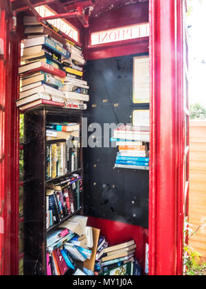 Un vecchio telefono rosso scatola utilizzata come un libro scambiare la posizione in un villaggio Wiltshire. Foto Stock