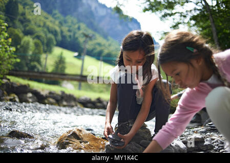 Due simpatici giovani ragazze a giocare insieme lungo un flusso di fiume in alto sulle montagne della Svizzera durante una vacanza estiva di sole Foto Stock